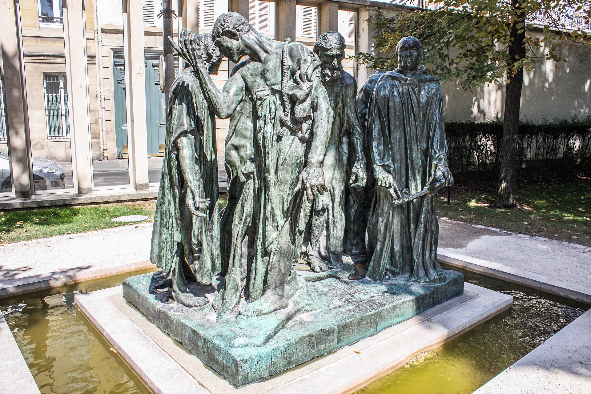 le monument des bourgeois de calais dans le jardin du musee rodin, six figures de bronze en tunique et la corde au cou sur une base basse, entouree d un bassin