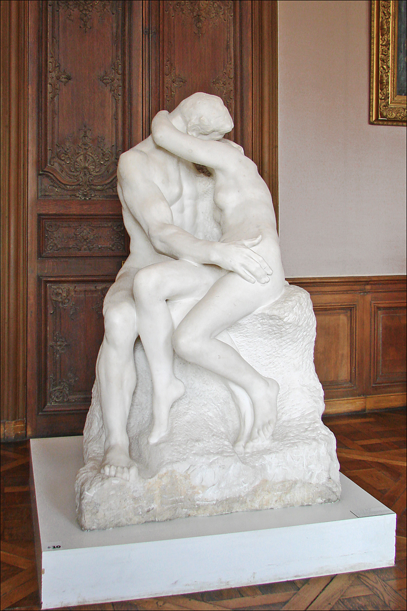 le baiser de rodin en marbre blanc dans la salle du musee, deux amants nus enlaces assis sur un bloc de pierre brute, devant des boiseries
