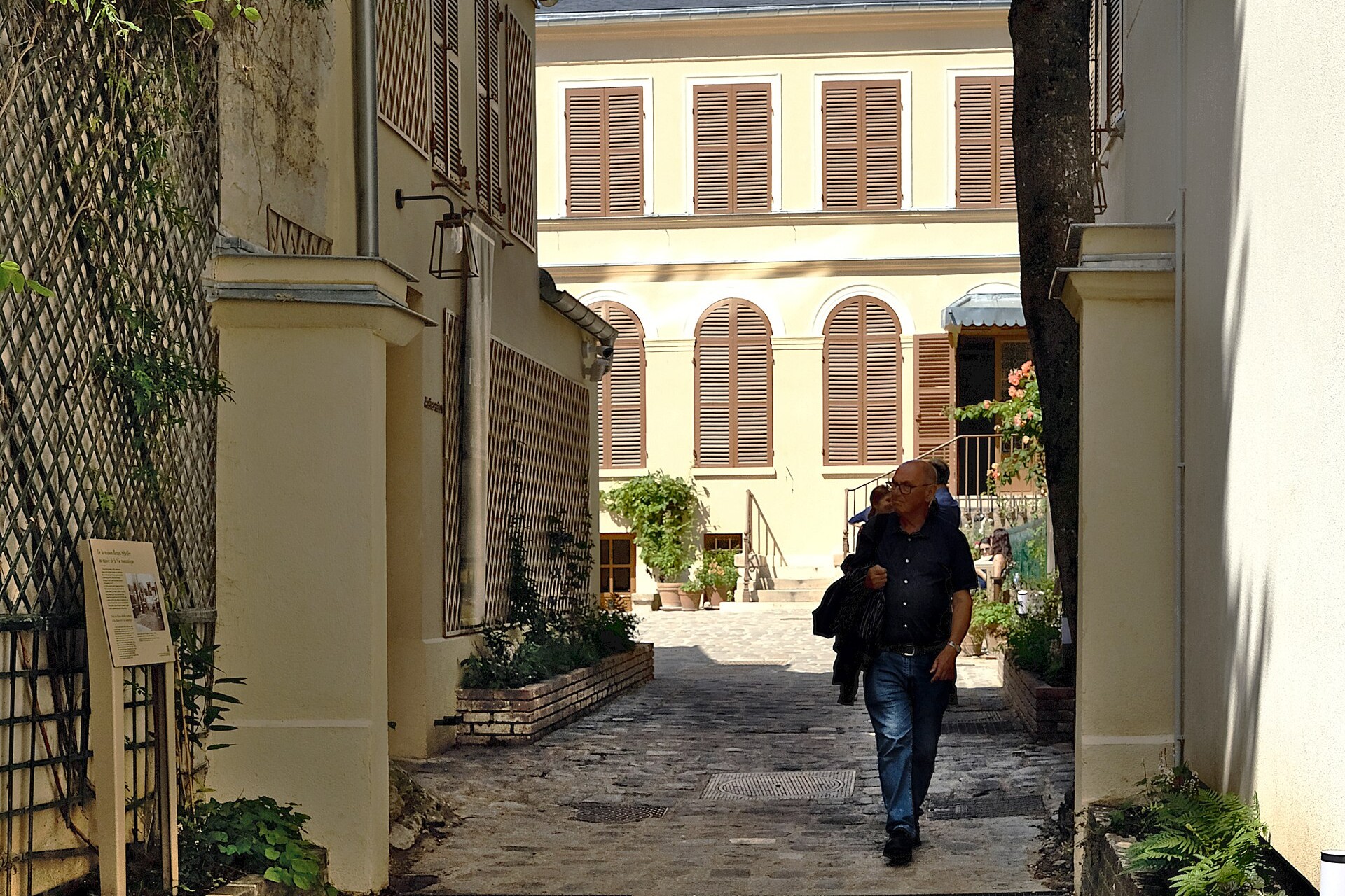 il cortile del musee de la vie romantique con la casa gialla a due piani, le finestre ad arco e le persiane bruno beige in fondo al viottolo