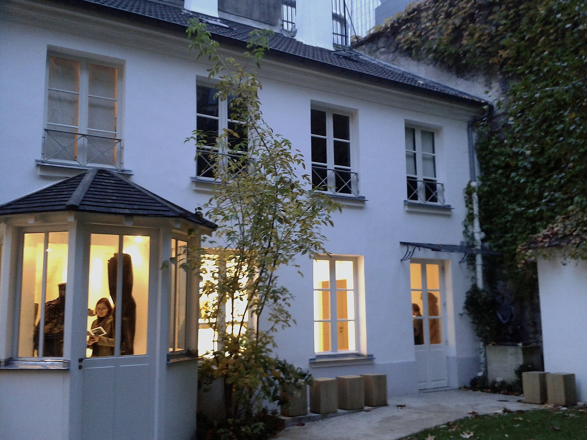 la maison blanche du musee zadkine vue du jardin a la tombee du jour, avec les fenetres eclairees, un pavillon vitre a gauche et le lierre sur le mur a droite