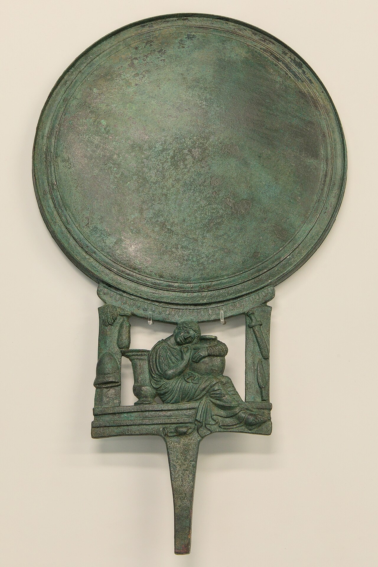 specchio greco in bronzo con il manico a figura femminile appoggiata a una colonnina