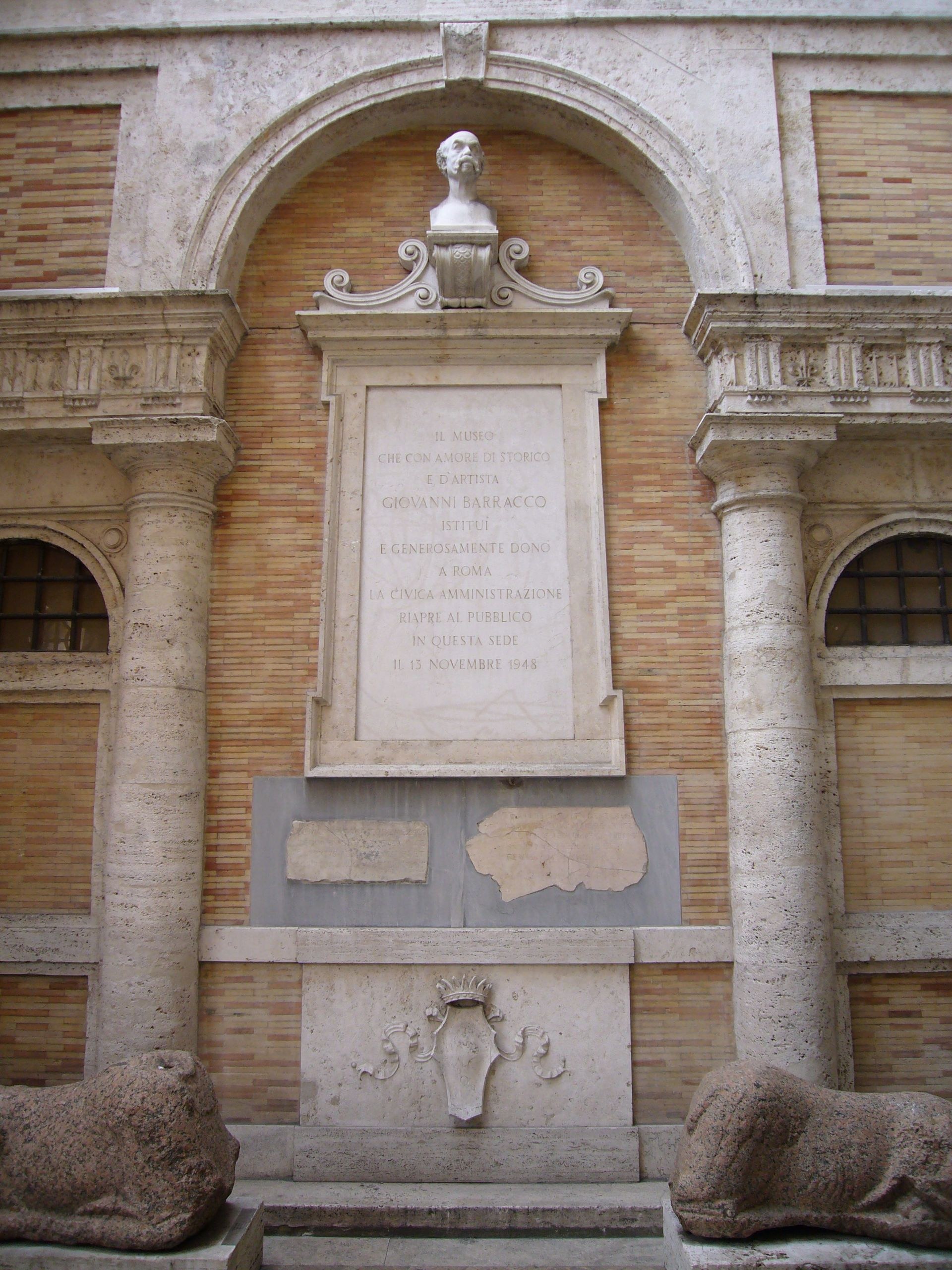 el monumento del patio de la piccola farnesina, con el busto de giovanni barracco arriba bajo el arco, la lapida que recuerda la donacion y dos leones de granito echados a los lados de la base