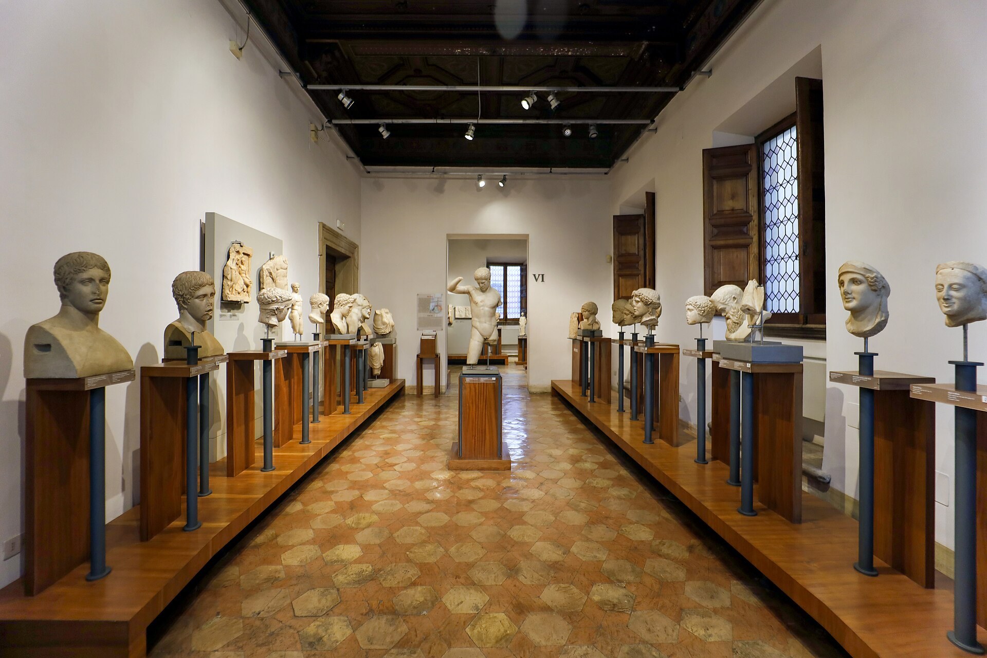 la sala del arte griego del museo barracco vista a lo largo, con dos filas de bustos antiguos sobre altos plintos de madera junto a las paredes