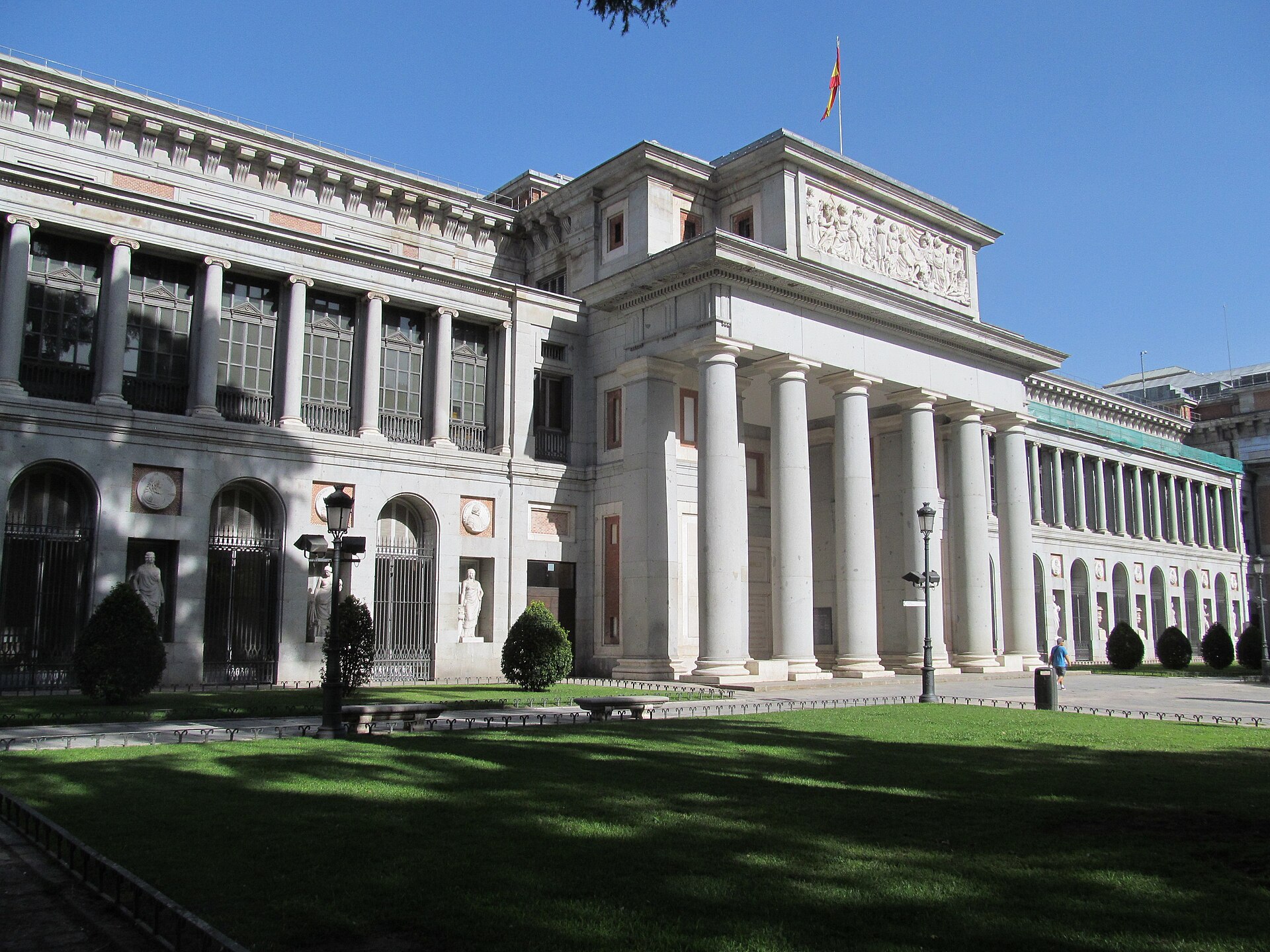 la facciata del museo del prado sul paseo del prado, con il portico di colonne al centro, le gallerie laterali e il prato davanti