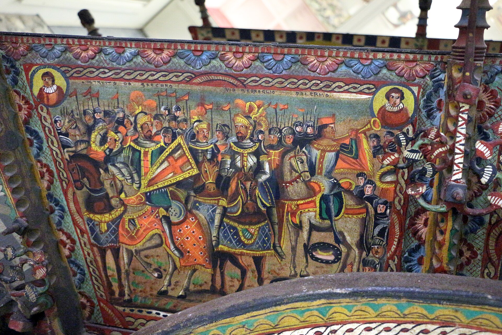 la sponda dipinta di un carretto siciliano al museo delle arti e tradizioni popolari, con una sfilata di cavalieri in armatura con lance e stendardi fra cornici di fiori