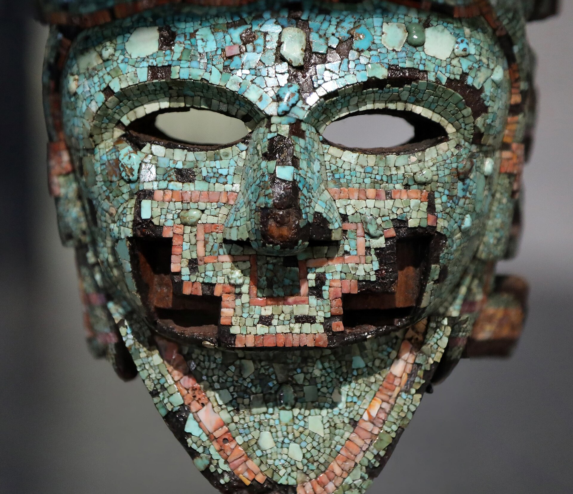 la maschera di turchese dei medici vista di fronte, un volto con occhi naso e bocca scavati inserito fra le mandibole di un serpente, con le gengive segnate da tessere rosse di conchiglia