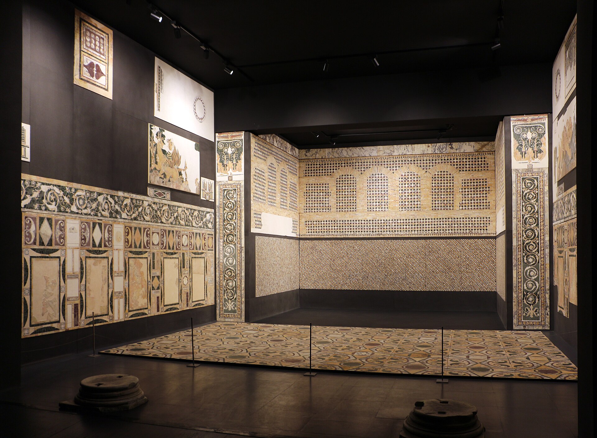 la sala ricostruita con le pareti in opus sectile dell edificio di porta marina a ostia, con i pannelli di marmo intarsiato illuminati nel buio del museo delle civilta