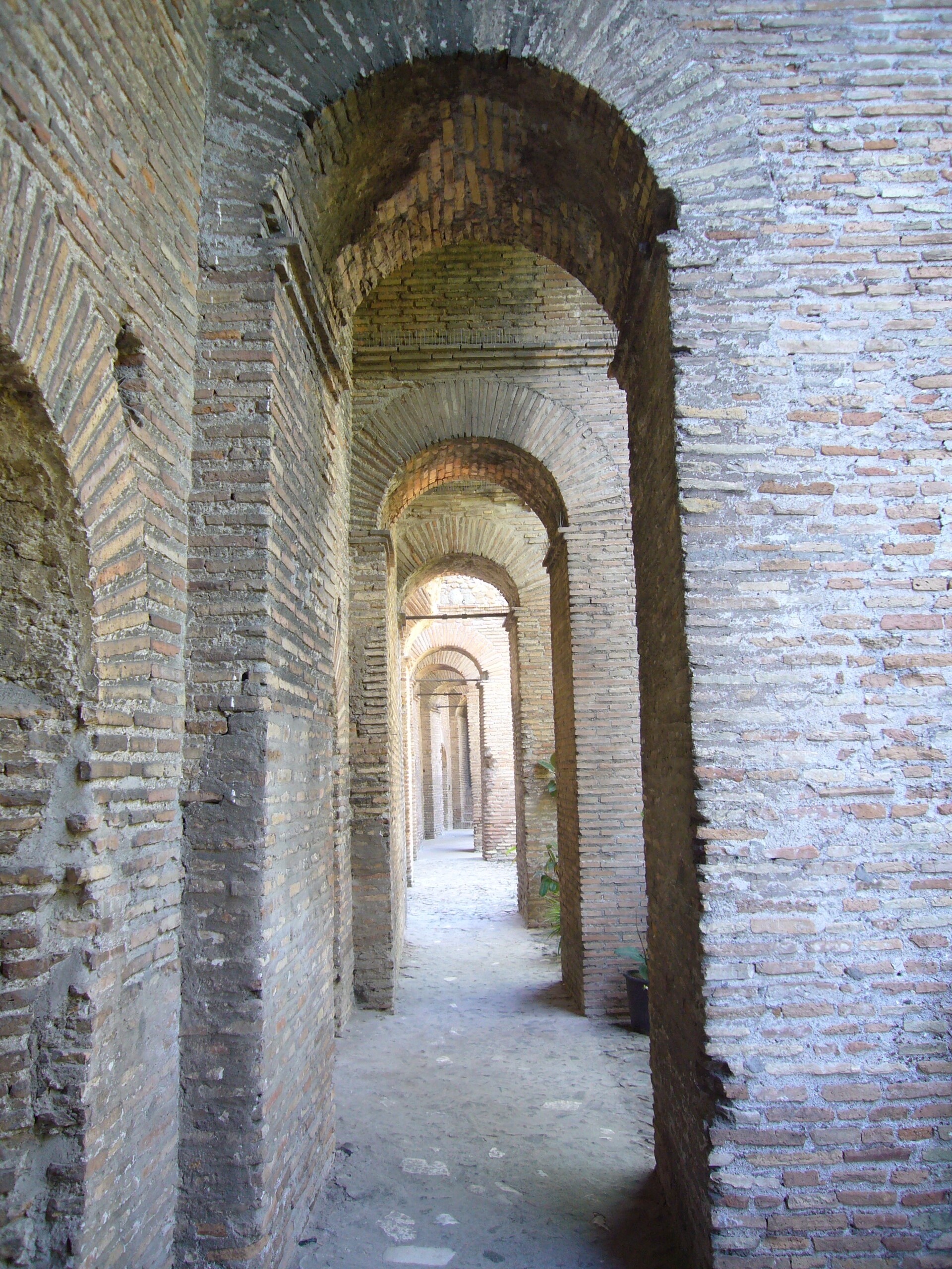 la galeria cubierta del adarve sobre las murallas aurelianas, una sucesion de arcos de ladrillo que se estrechan hacia el fondo, el muro macizo a la izquierda y el suelo de tierra batida