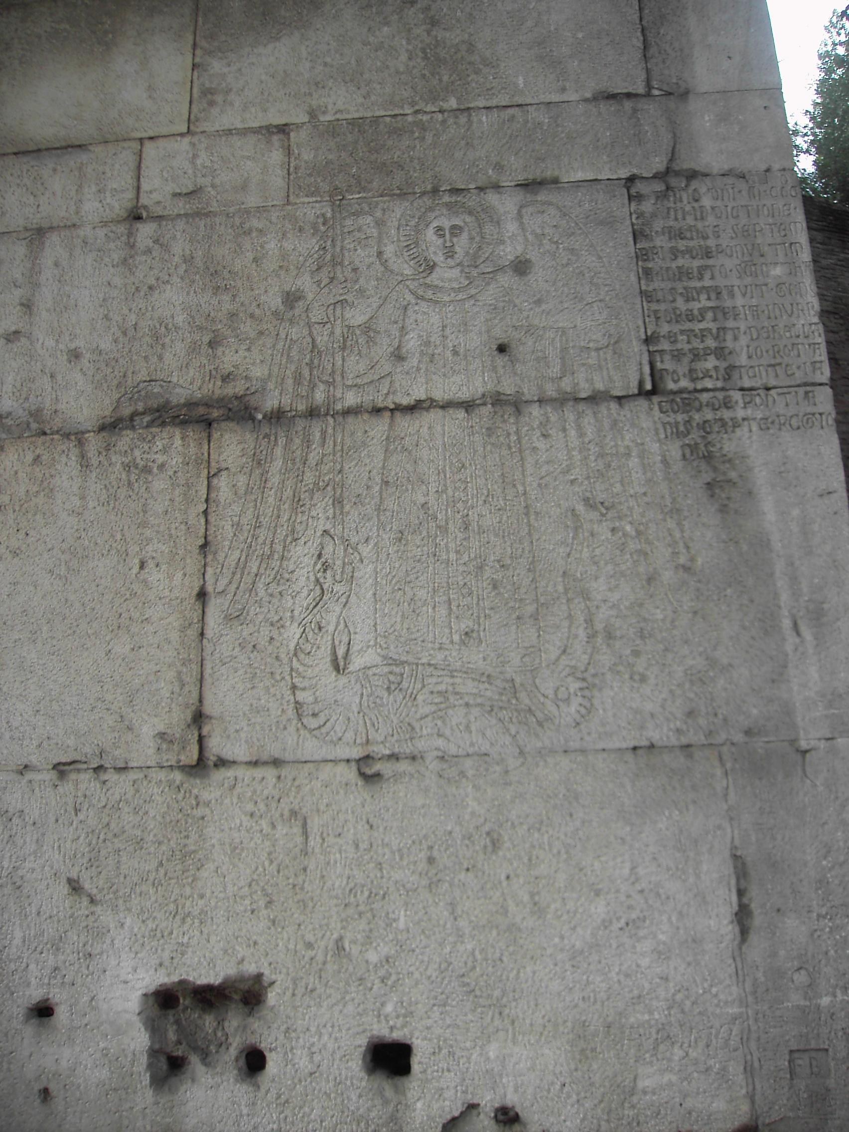 el grafito medieval en la jamba de porta san sebastiano, con el arcangel con nimbo y las alas desplegadas que clava la lanza en un dragon enroscado y la inscripcion gotica grabada al lado