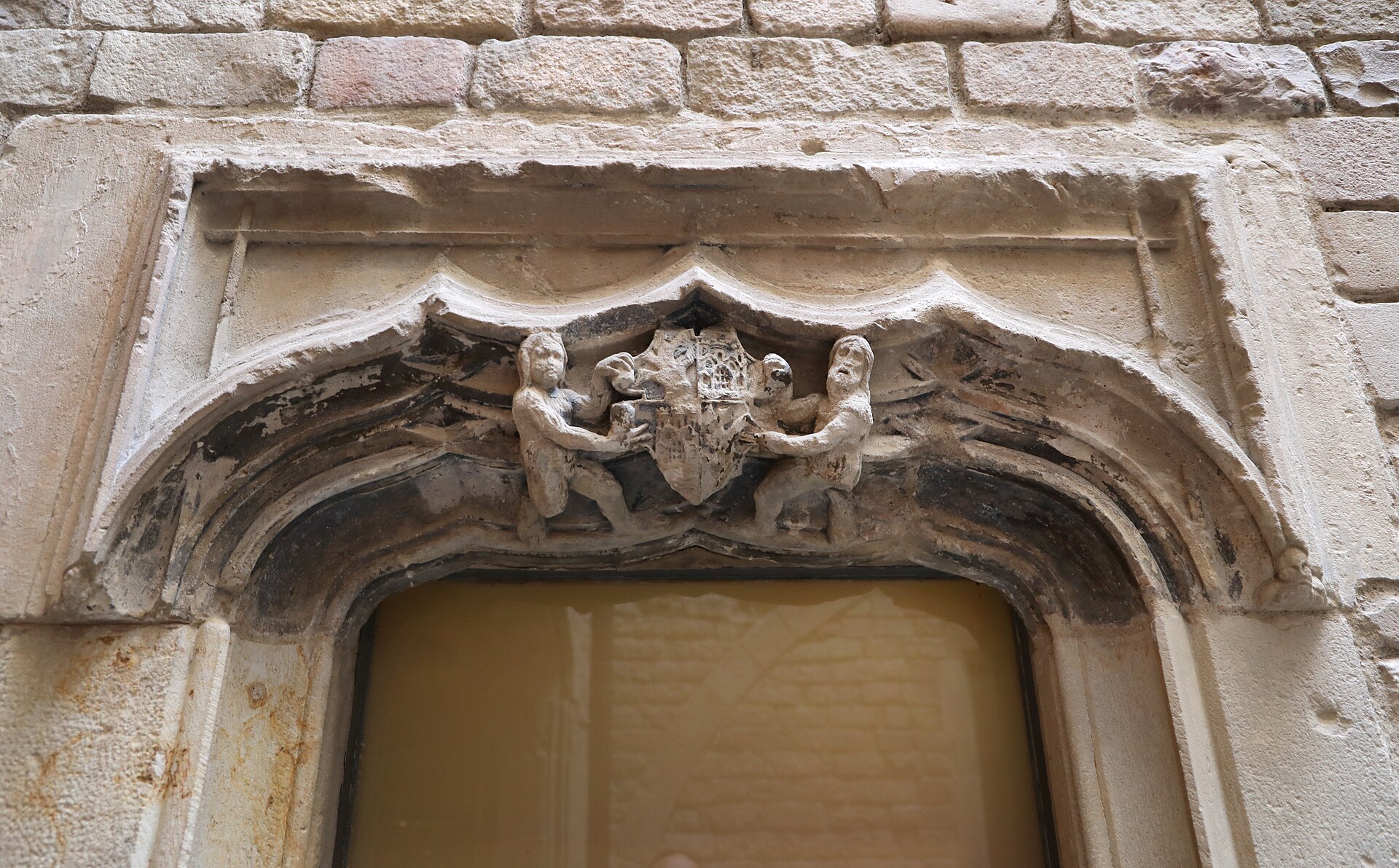 una finestra del palau aguilar con un arco scolpito e, sopra, uno stemma retto da due putti di pietra