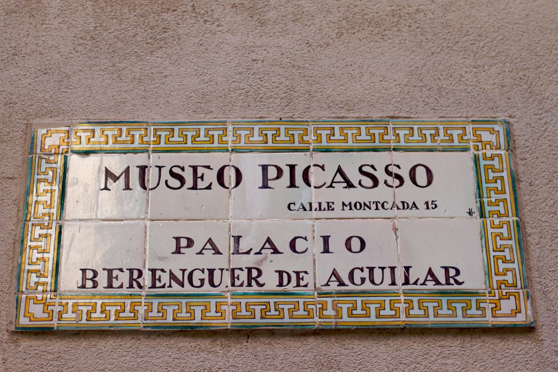 una targa di piastrelle con la scritta museo picasso, calle montcada 15, palacio berenguer de aguilar, dentro una cornice decorata gialla e verde