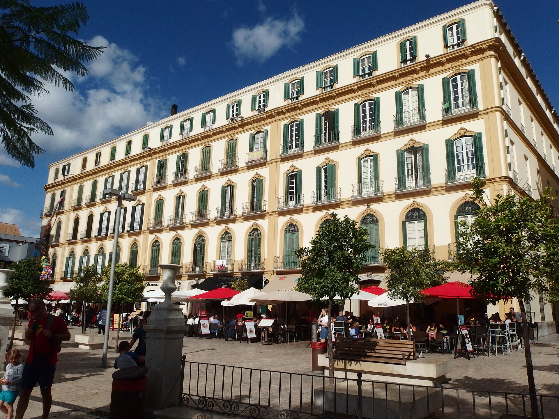 il grande palazzo giallo e bianco di plaza de la merced a malaga, dove si trova la casa natale di picasso, con i tavolini all’aperto davanti