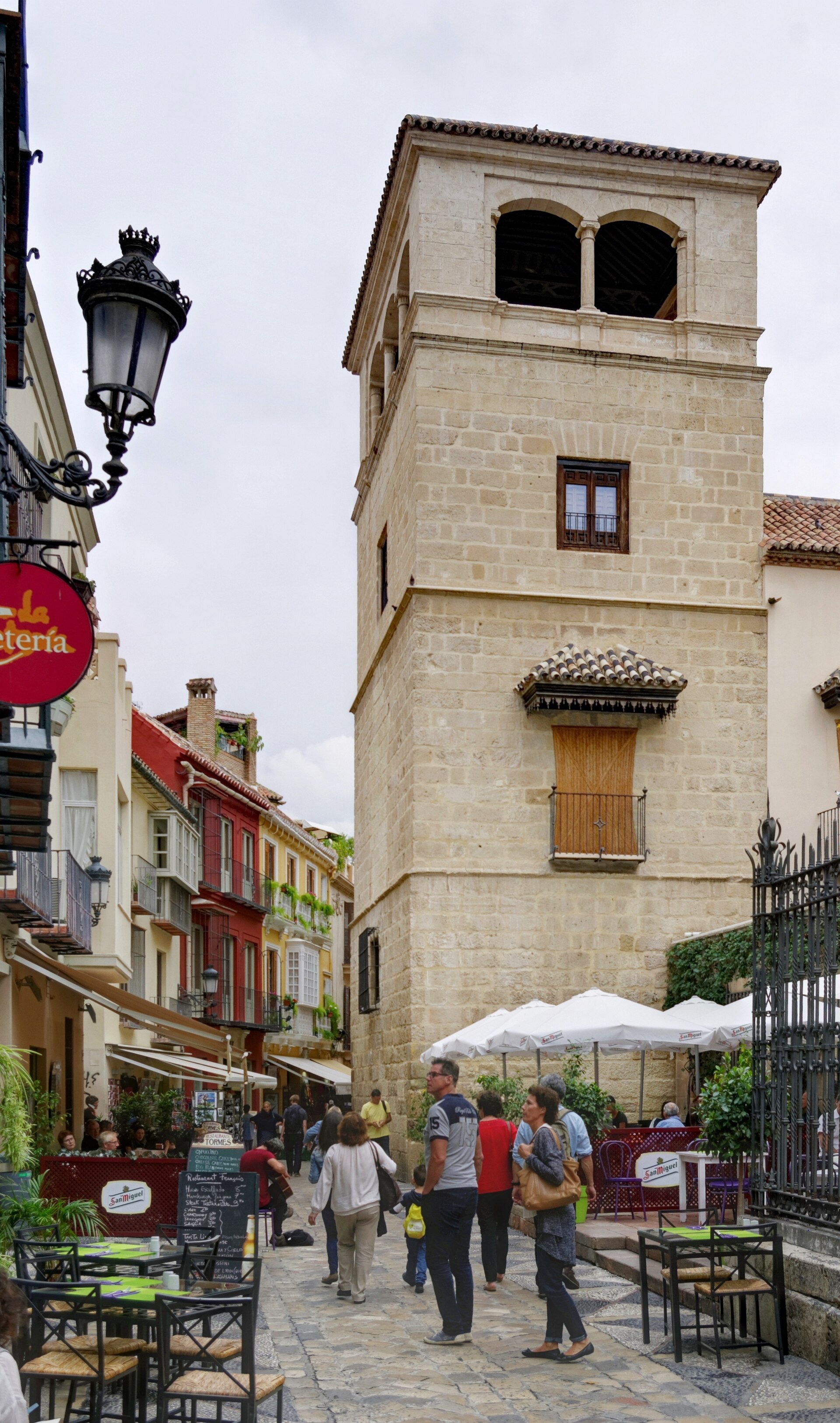 la torre del palacio de buenavista che si alza sopra calle san agustin a malaga, con i lampioni e la gente seduta ai tavolini della strada