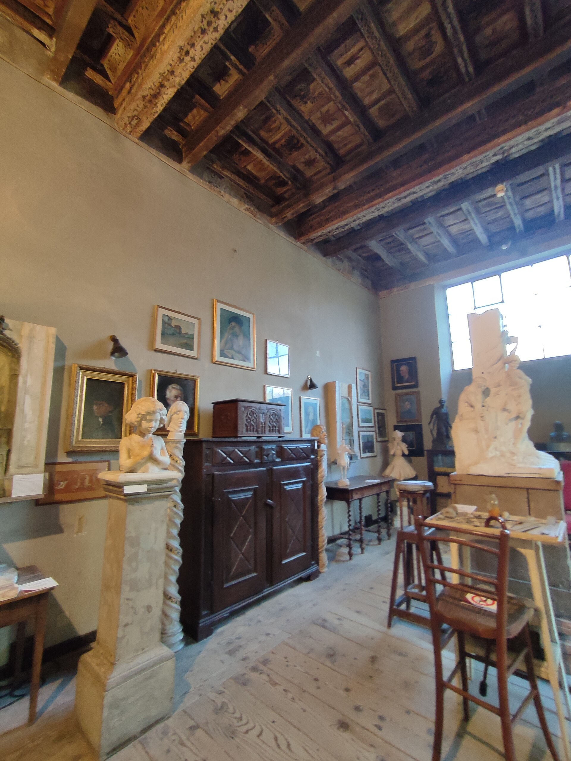 el taller de pietro canonica con el techo de vigas de madera, los caballetes de trabajo, los modelos de escayola apoyados y los muebles oscuros junto a las paredes