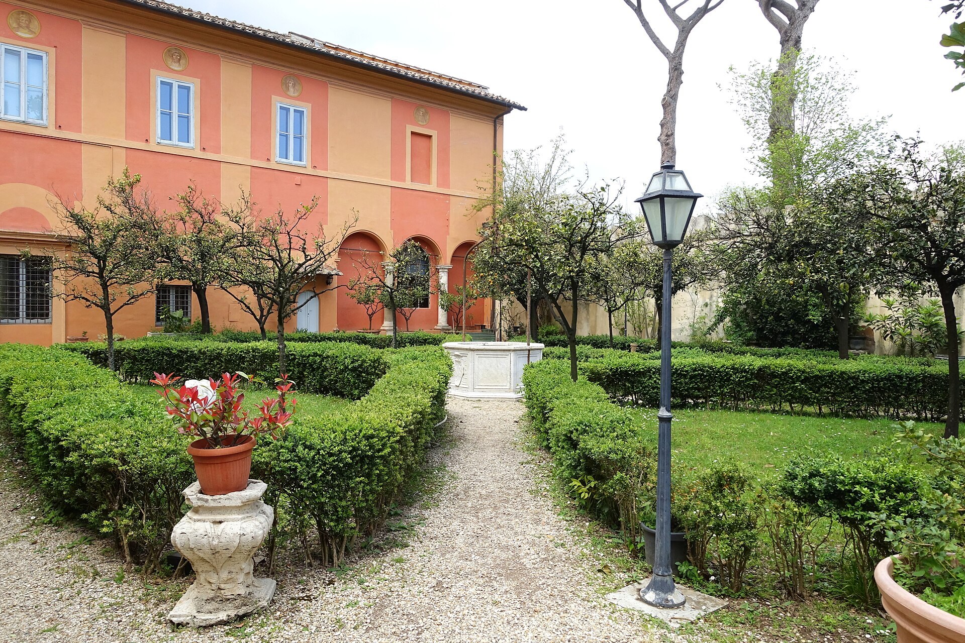 la fortezzuola vista desde su jardin a la italiana, con la fachada rosa y los arcos de la planta baja, los setos de boj recortados y una farola en primer plano