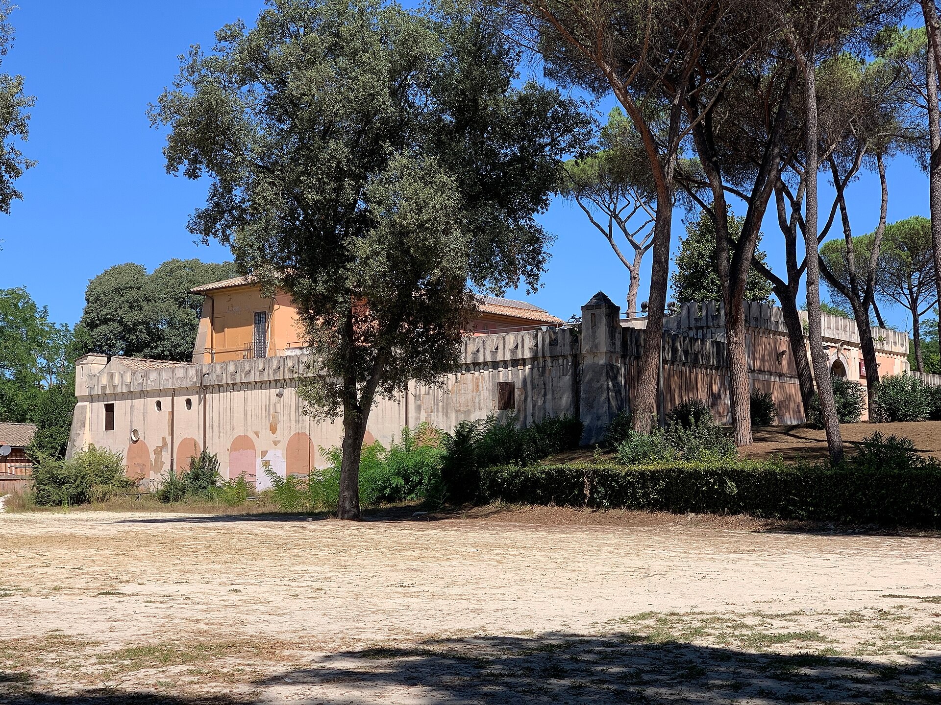 la fortezzuola de villa borghese vista desde fuera, con el muro almenado de falso medieval, los pinos pineos alrededor y la explanada de tierra batida delante
