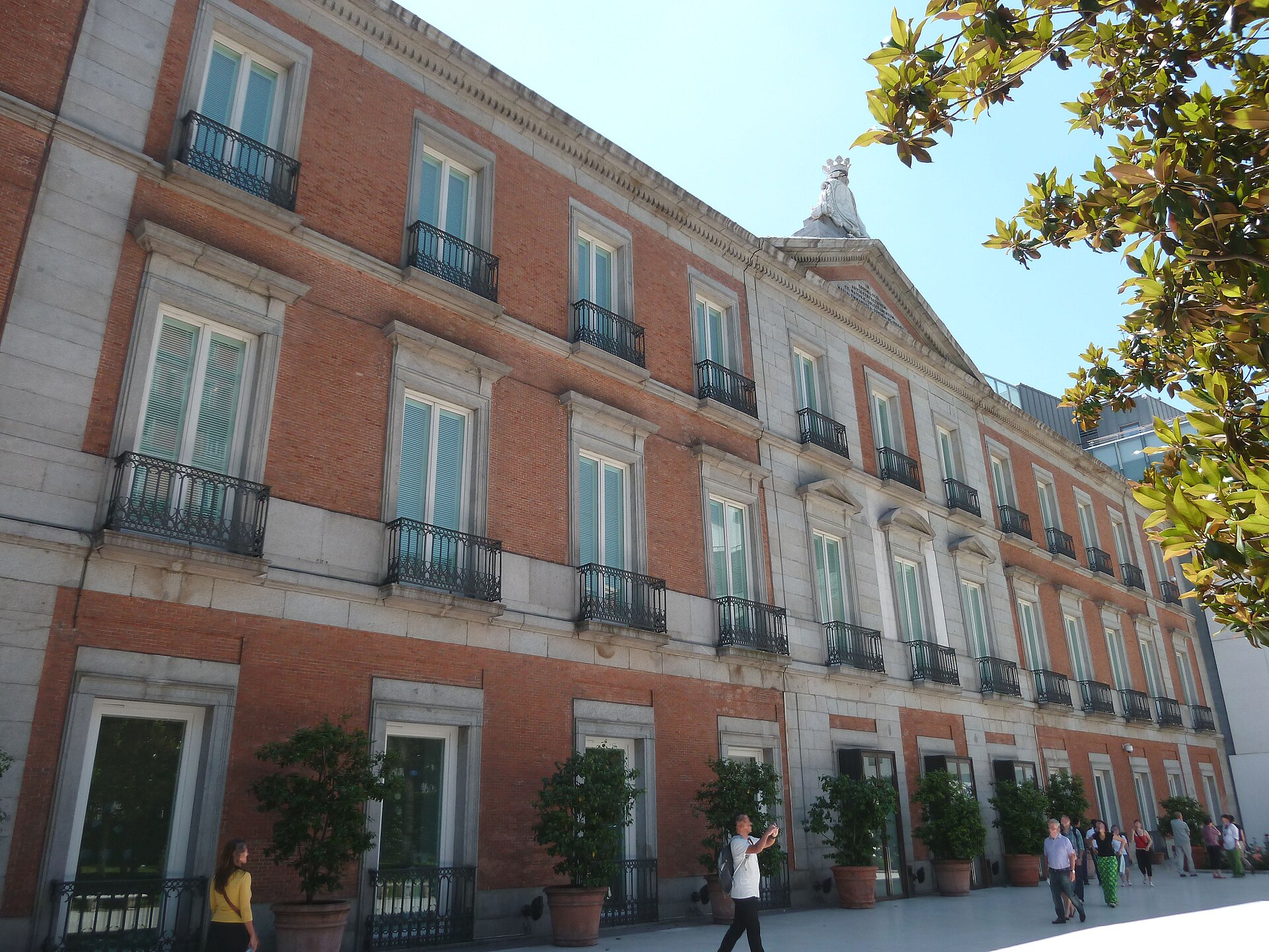 the façade of the villahermosa palace, home of the thyssen-bornemisza museum in madrid, in red brick and pale stone, with small trees in large pots along its base