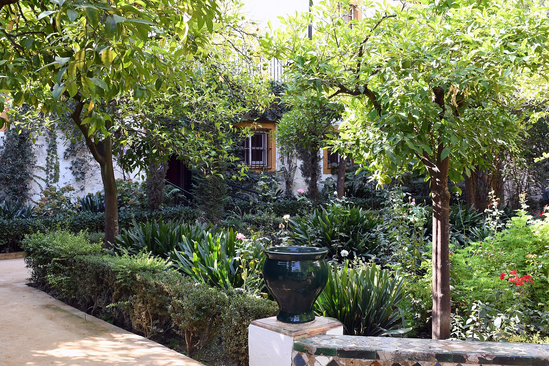 il giardino dei limoni del palacio de las duenas, con gli alberi, le aiuole fiorite, un vaso di ceramica verde e un vialetto