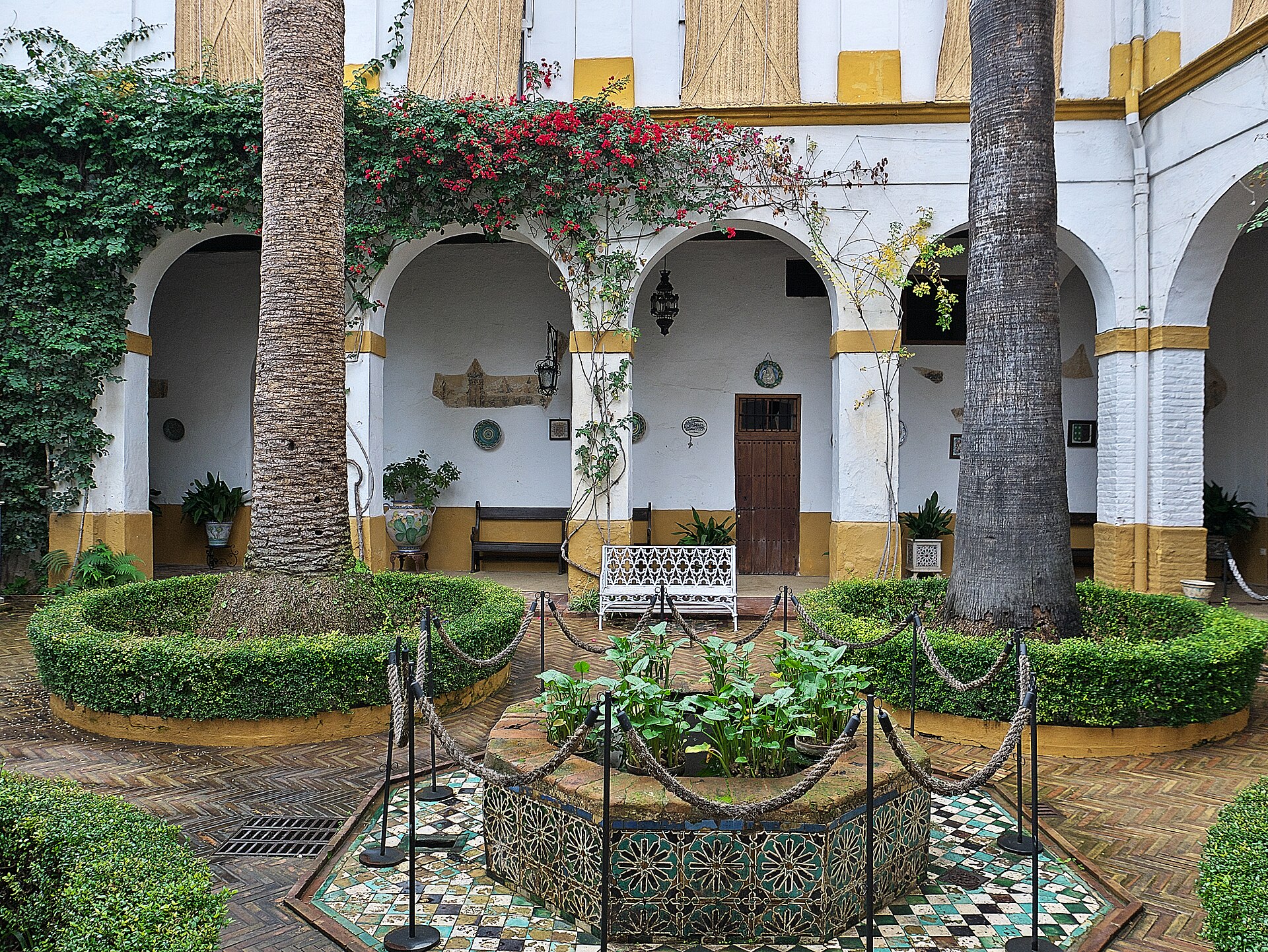 il patio del aceite del palacio de las duenas, con una fontana di azulejos al centro, le aiuole rotonde, le palme e le gallerie bianche e gialle