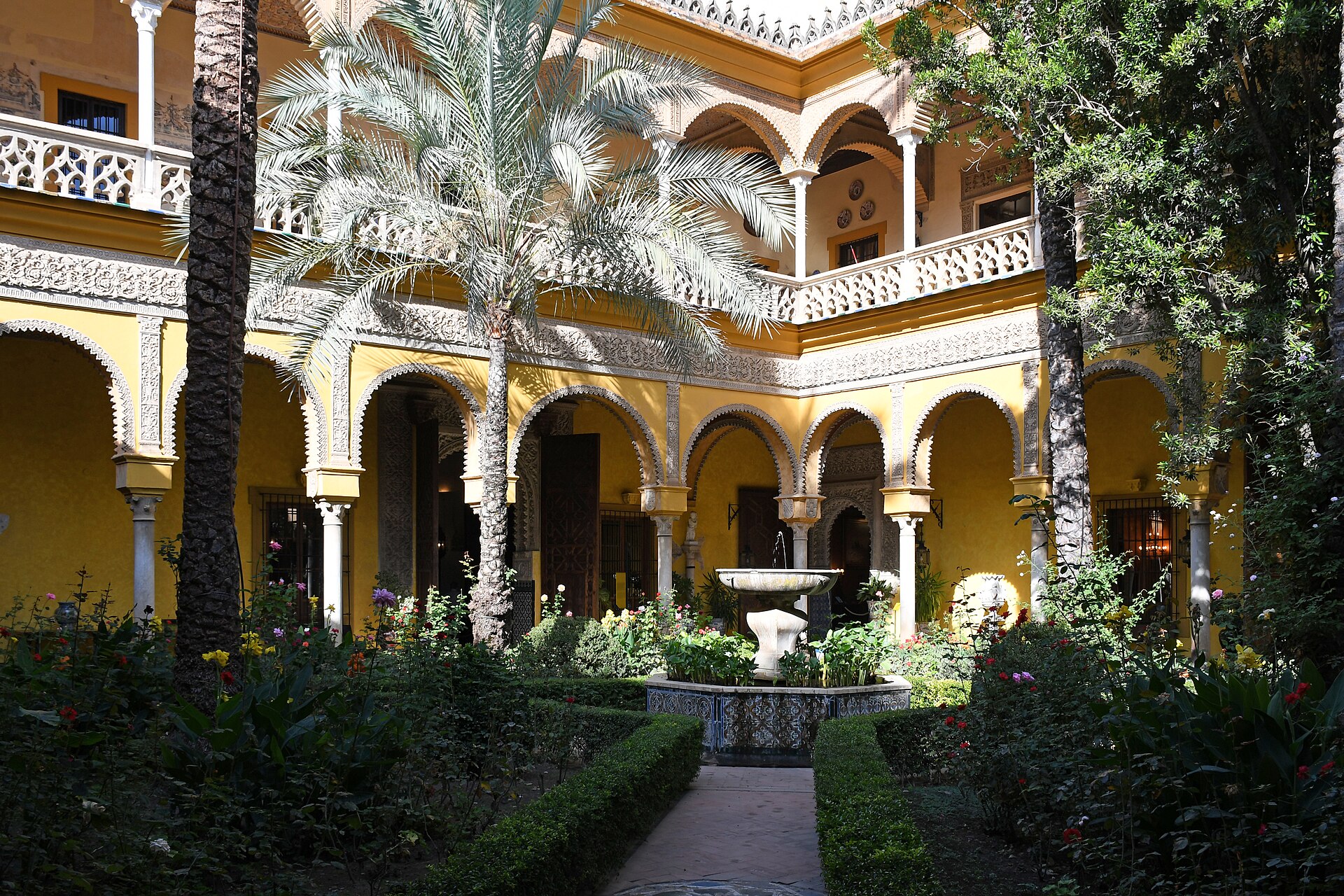 il patio principale del palacio de las duenas a siviglia, con la fontana al centro, le palme, le siepi e le gallerie gialle e bianche su due piani