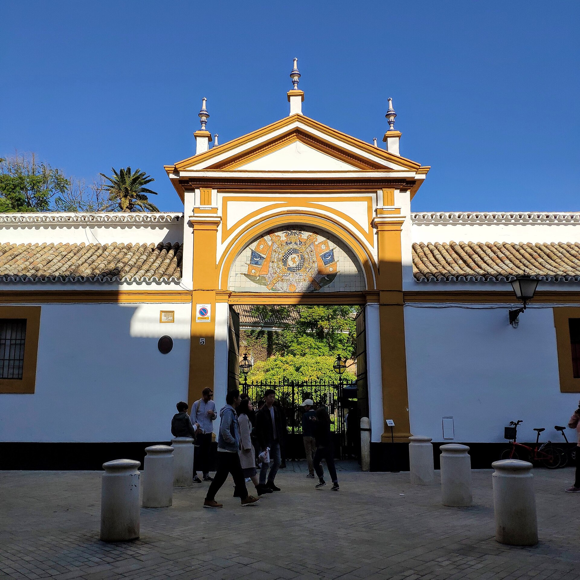 il portale d’ingresso del palacio de las duenas su calle duenas, bianco e giallo, con uno stemma di azulejos sopra l’arco e il giardino che si vede oltre il cancello