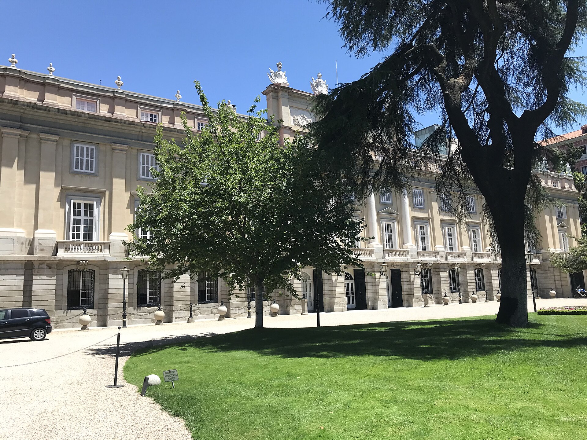la facciata principale del palacio de liria a madrid, lunga e color sabbia, con le colonne, le balaustre e le statue sul tetto, dietro un prato e un grande cedro