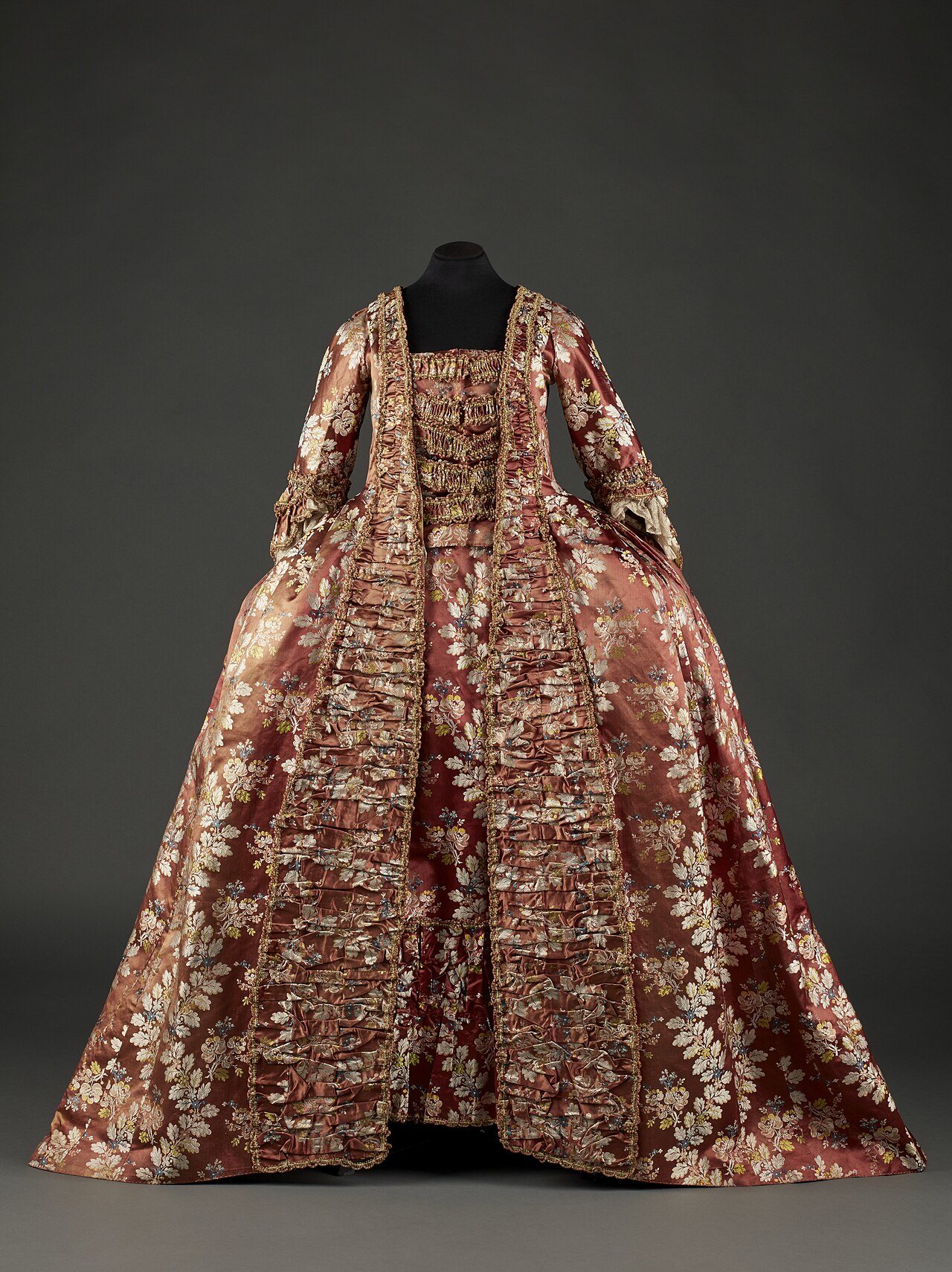 una robe a la francaise in seta broccata rosa antico con motivi floreali argentati, con le larghe panier ai fianchi e le balze arricciate sul davanti