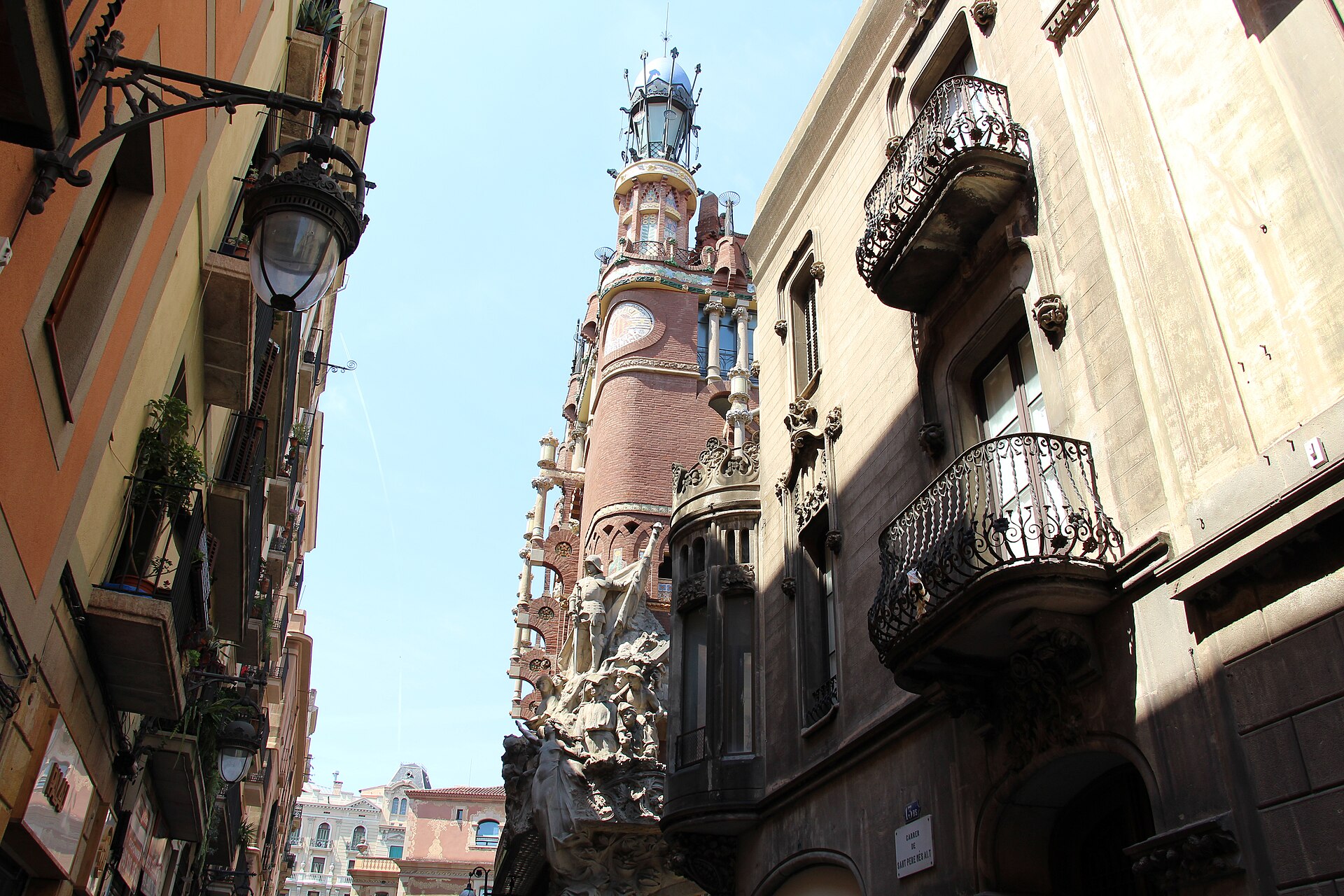 la facciata del palau de la musica catalana vista dal fondo di una strada stretta, fra balconi in ferro e lampioni