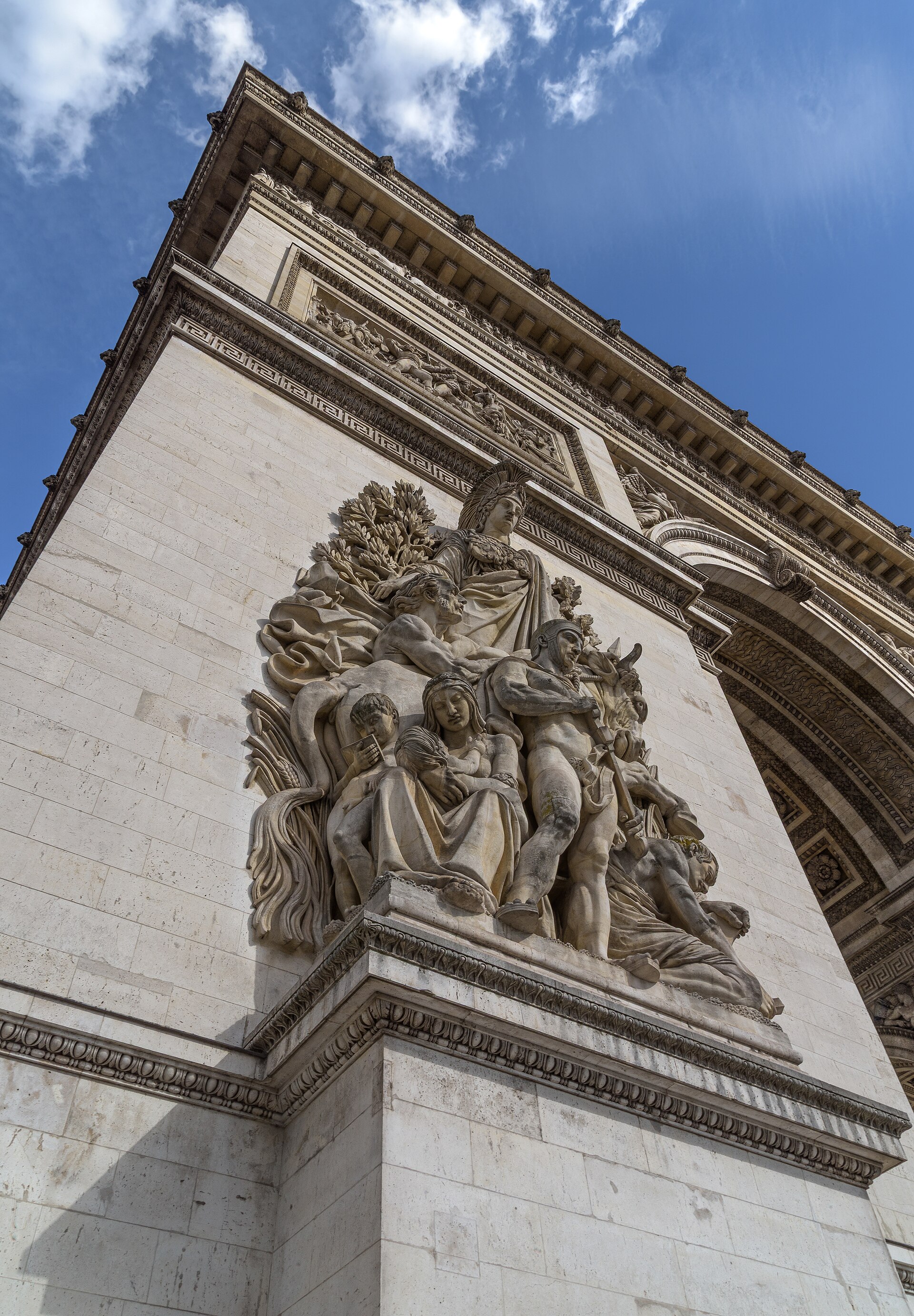 un gruppo di statue scolpito sul pilastro dell’arco di trionfo di parigi, visto dal basso contro il cielo, con una figura femminile coronata in alto e un guerriero che rinfodera la spada
