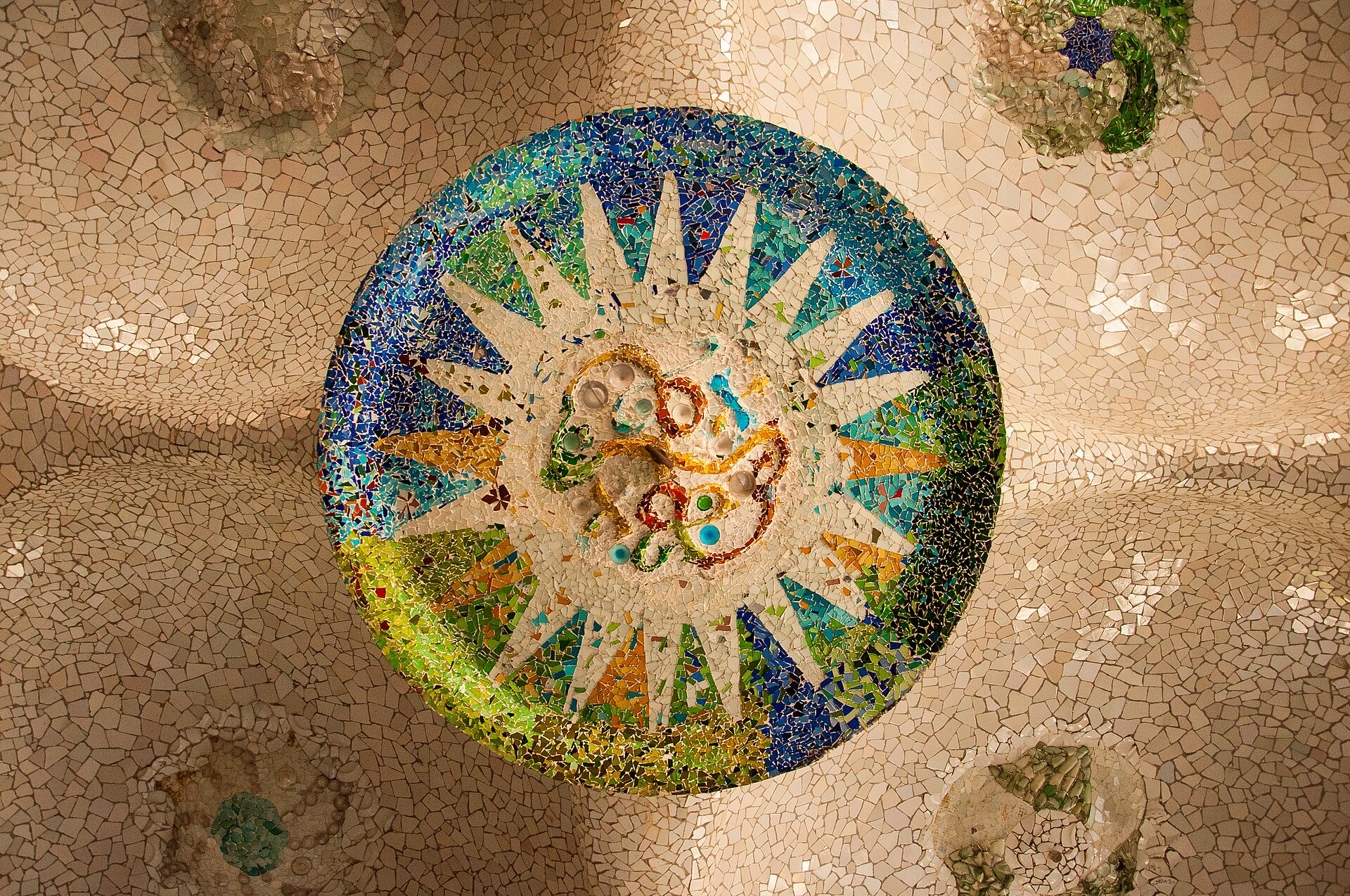 un medaglione di cocci colorati a forma di sole sul soffitto bianco della sala ipostila di park guell
