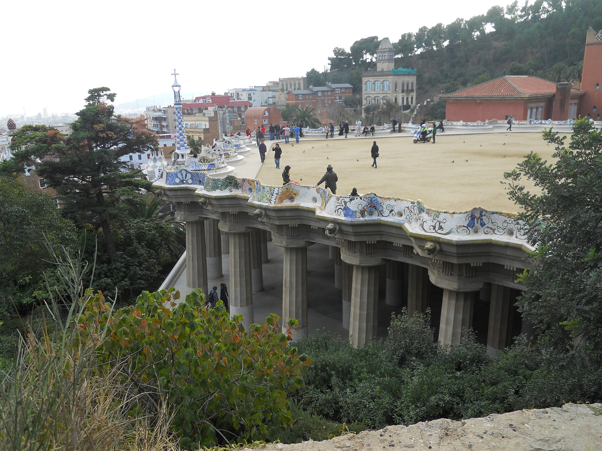la piazza di park guell vista dal basso, sorretta dalle colonne della sala ipostila e bordata dalla panca a mosaico