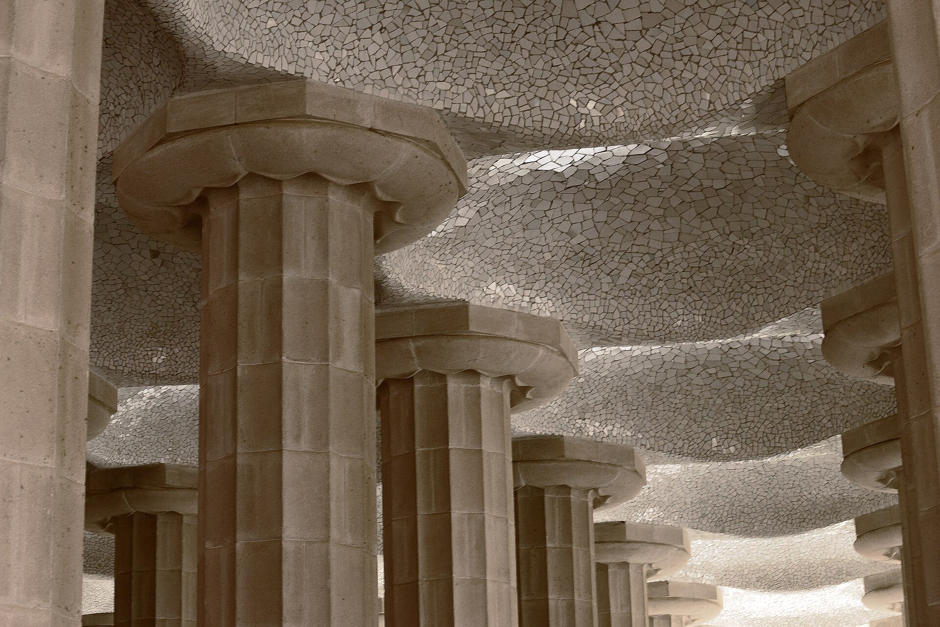 le colonne scanalate della sala ipostila di park guell sotto un soffitto bianco a cupolette di cocci di ceramica