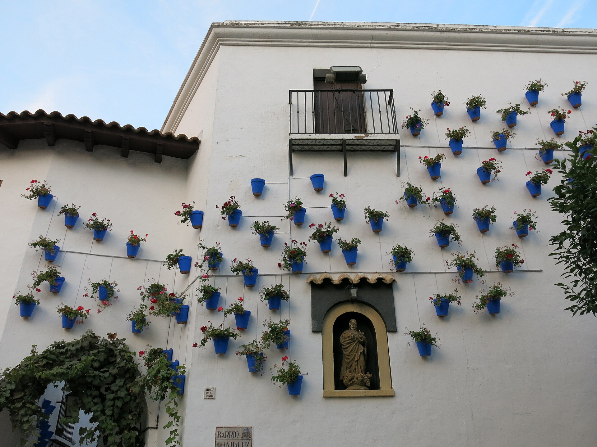 un muro bianco del quartiere andaluso del poble espanyol coperto di vasi azzurri con gerani rossi, attorno a una nicchia con una statua