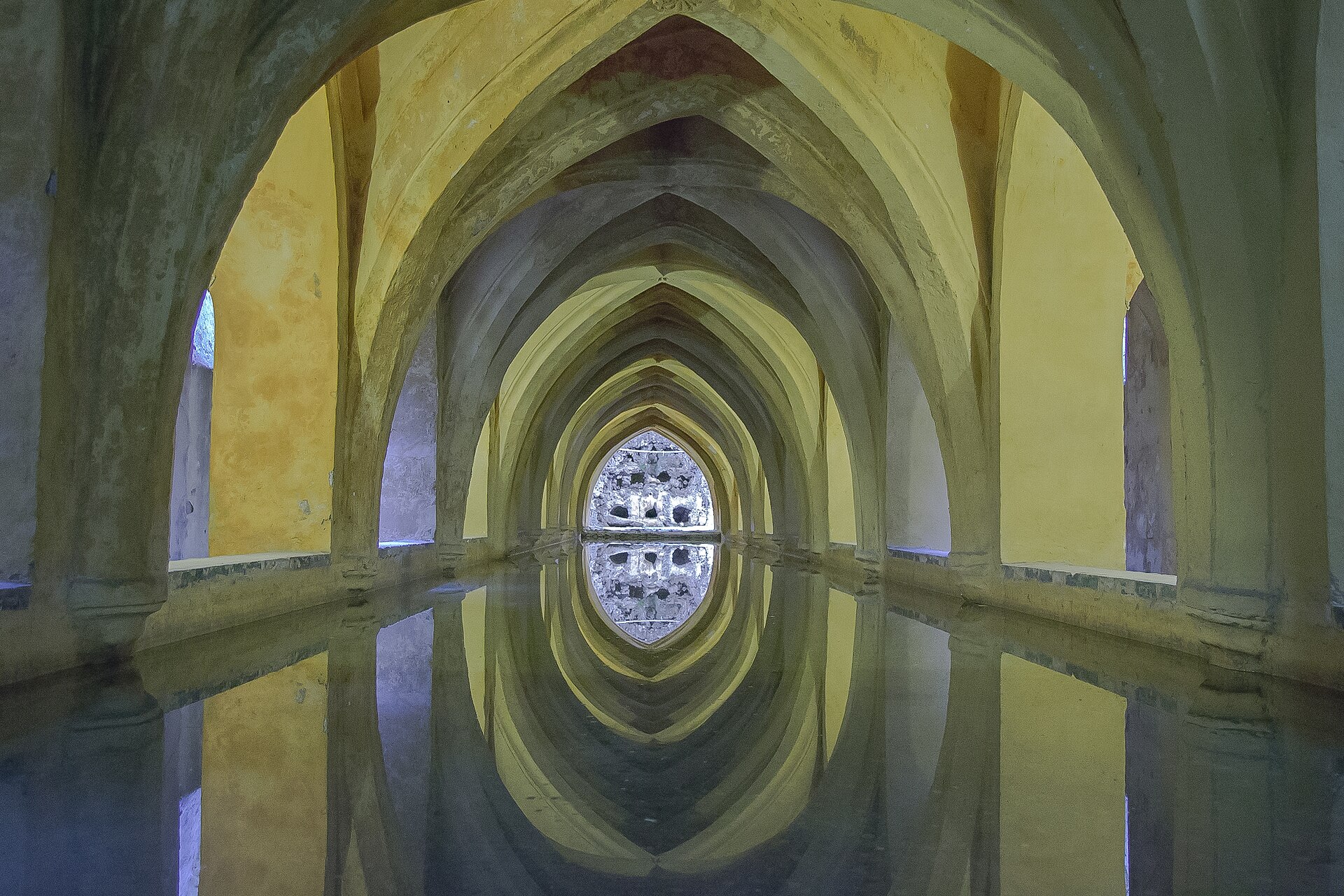 i banos de dona maria de padilla nel real alcazar di siviglia, una galleria a volte a sesto acuto con una vasca d’acqua che riflette gli archi