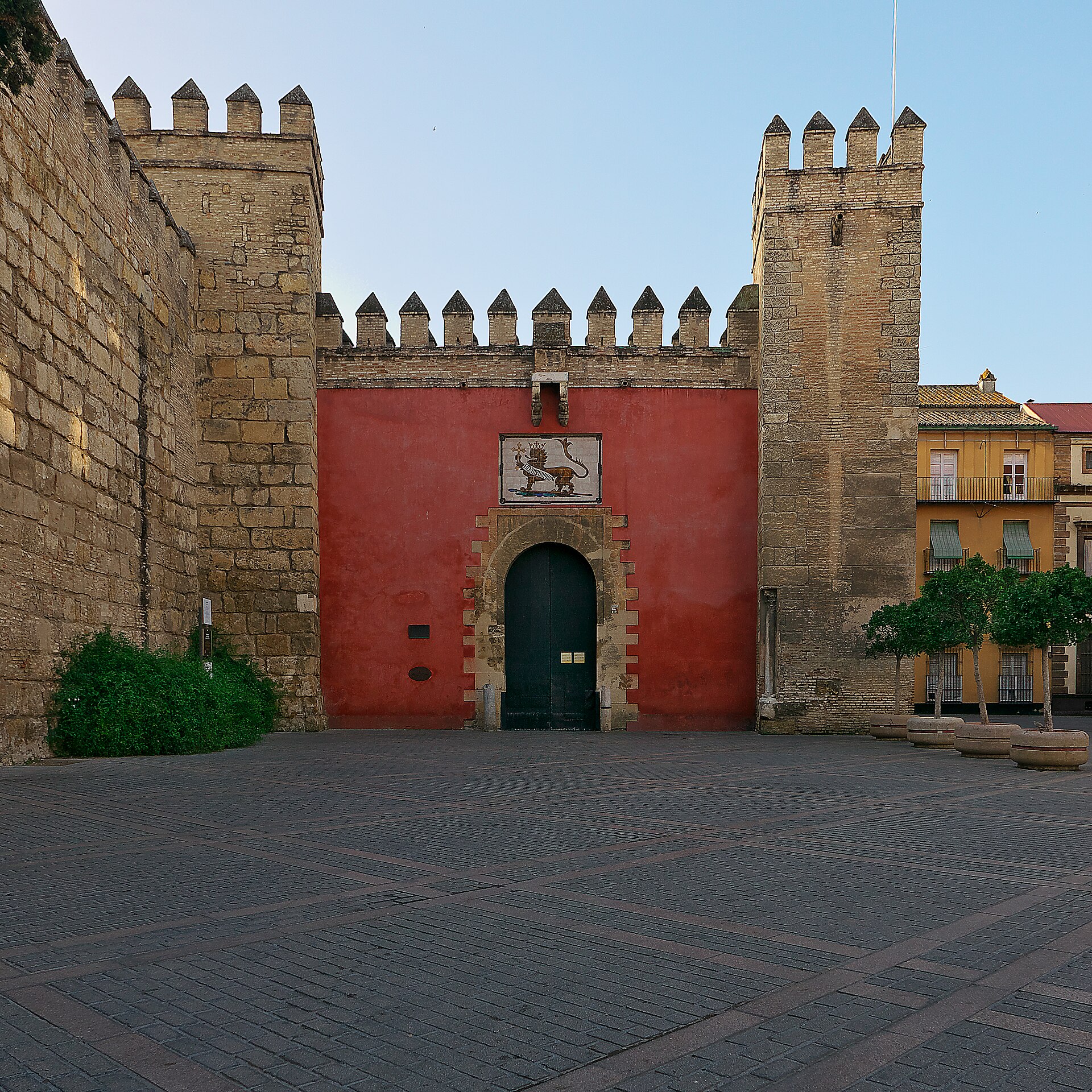 la puerta del leon del real alcazar di siviglia, un portale nella muraglia merlata dipinta di rosso con un leone sopra l’arco