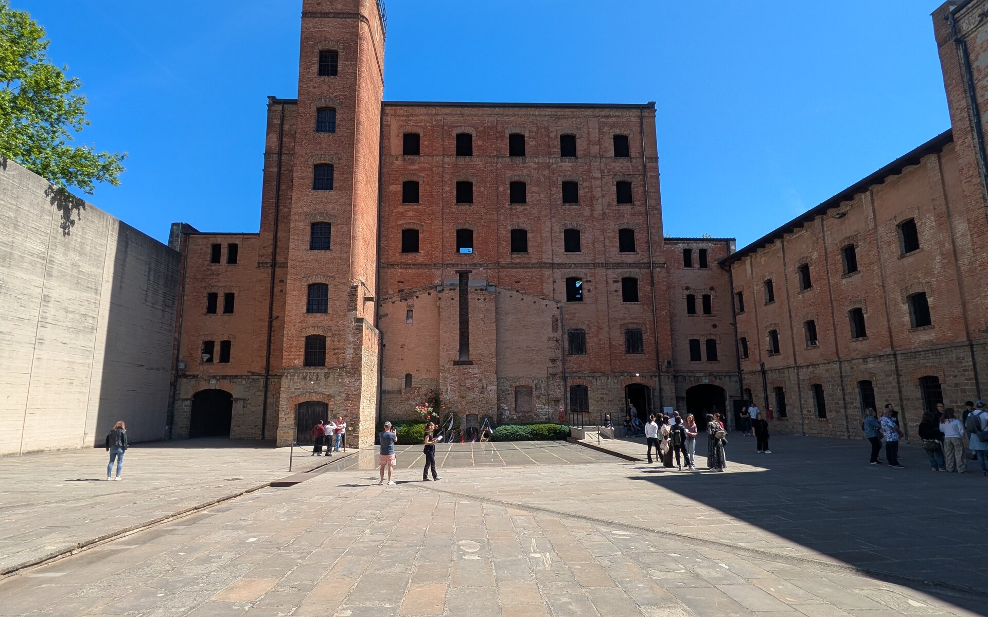 il cortile della risiera di san sabba con gli edifici industriali in mattoni la stele in acciaio e il muro di cemento