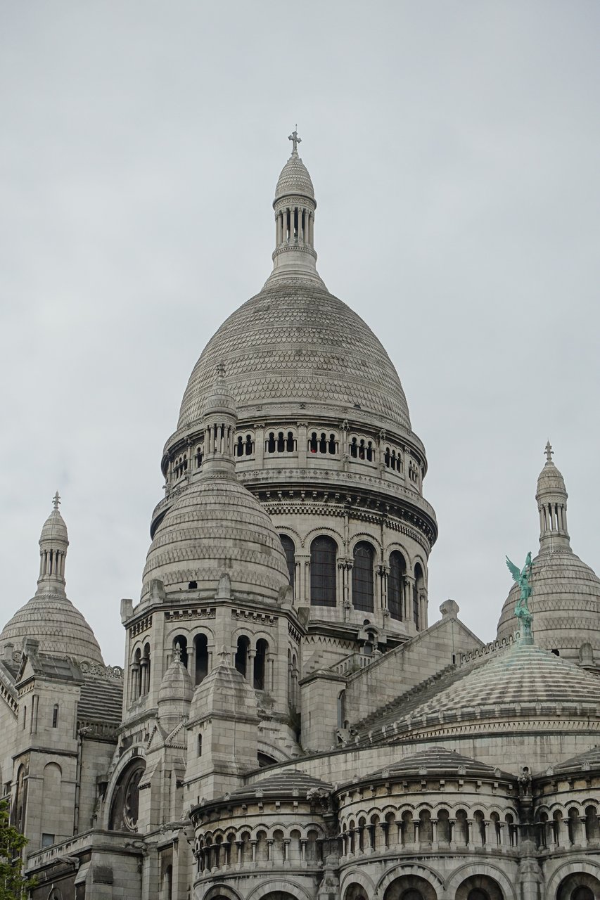 la cupola centrale del sacre coeur vista da vicino, con la lanterna sormontata da una croce, le cupole minori ai lati e una delle statue equestri in bronzo visibile sul tetto in primo piano