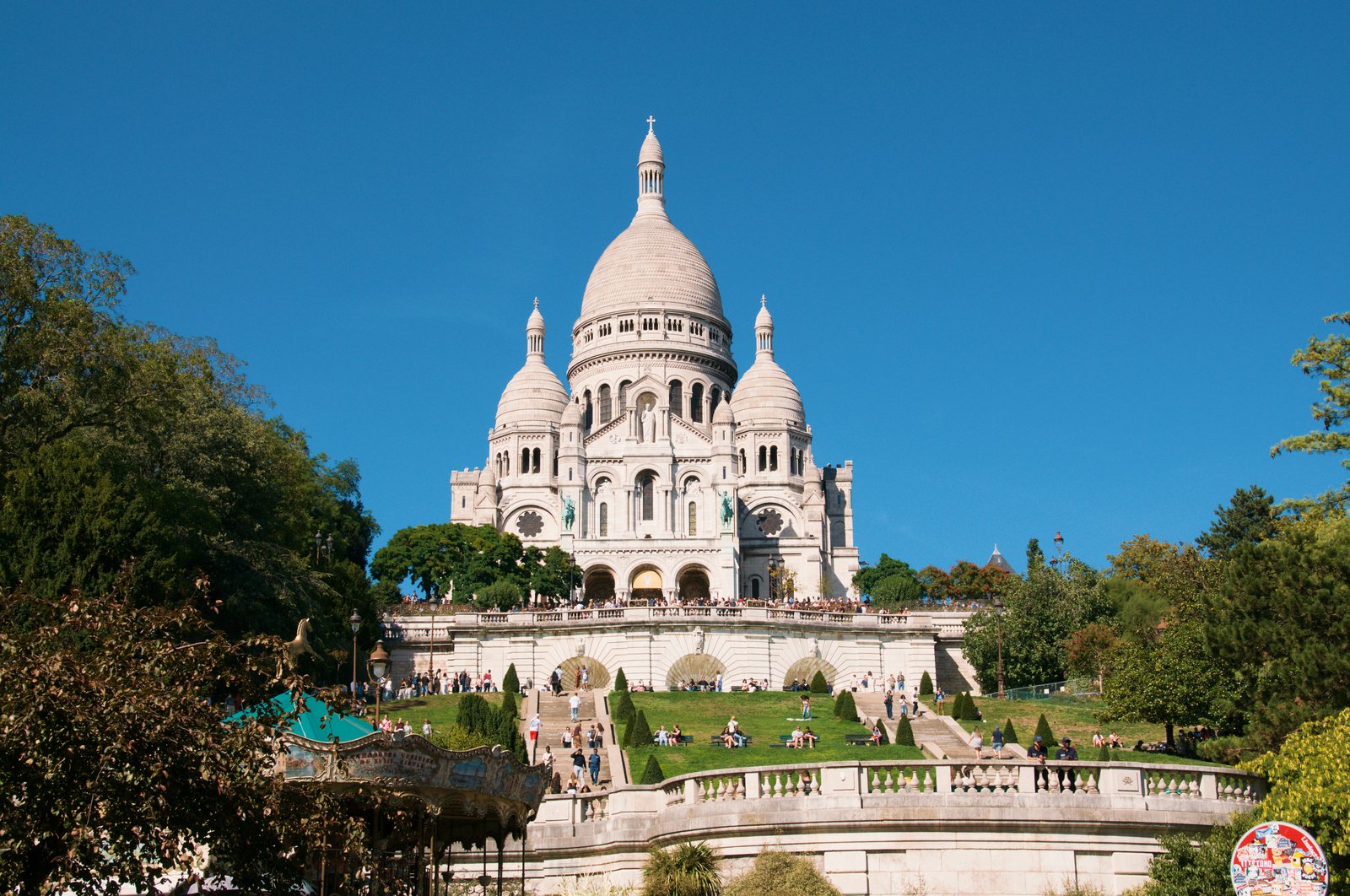 la basilica del sacre coeur vista dal basso della scalinata, con la cupola bianca centrale, le cupole minori e il prato verde in primo piano sotto un cielo azzurro