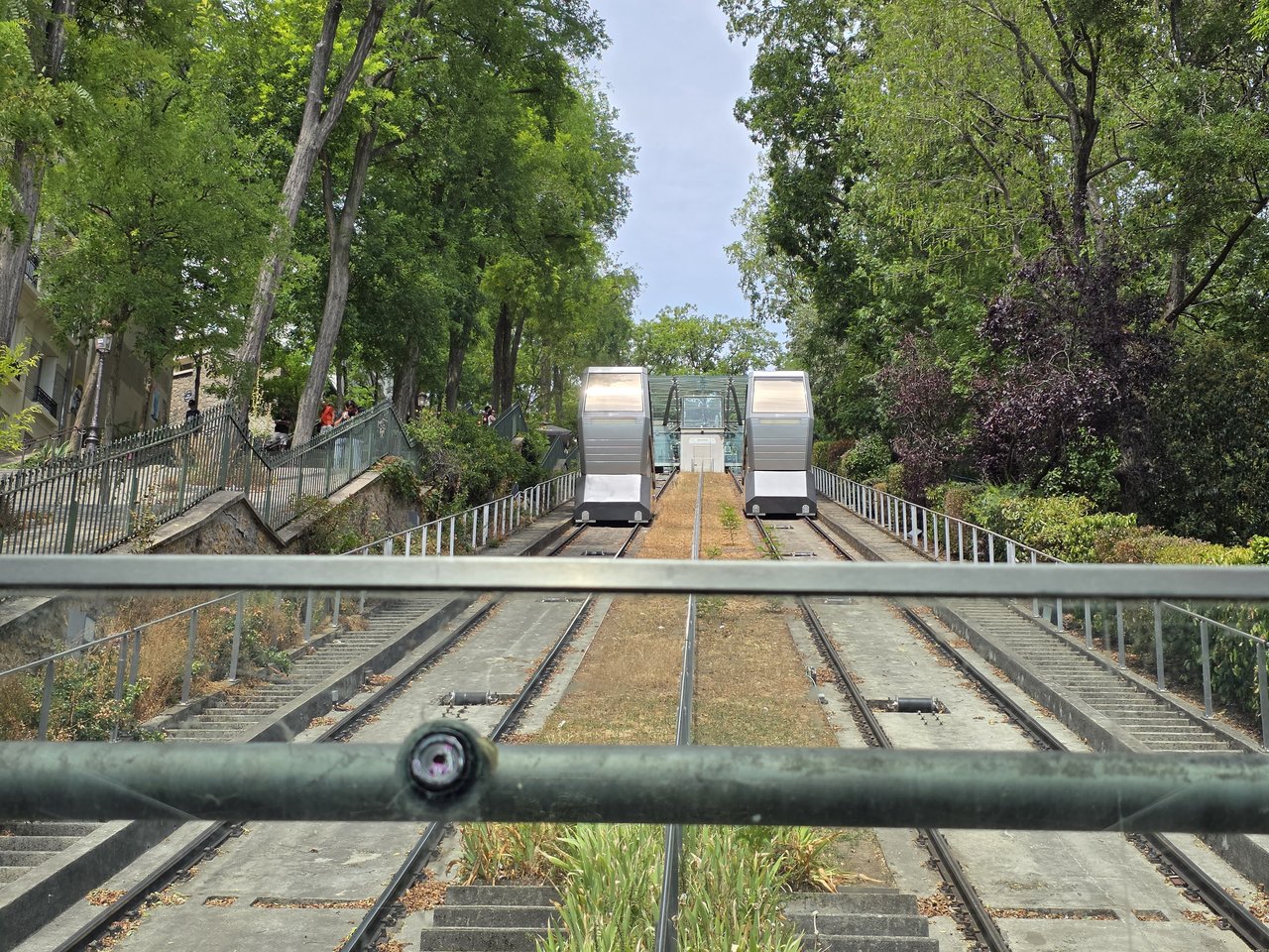 le due cabine della funicolare di montmartre viste dal basso lungo i binari in discesa, circondate dal verde degli alberi