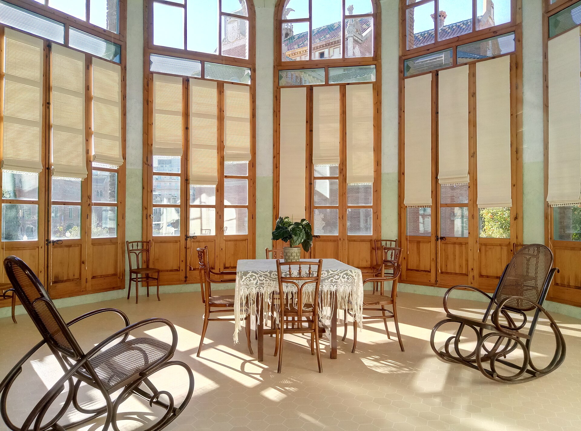 la sala di giorno del padiglione di sant rafael a sant pau, con finestre alte, tende chiare e sedie a dondolo