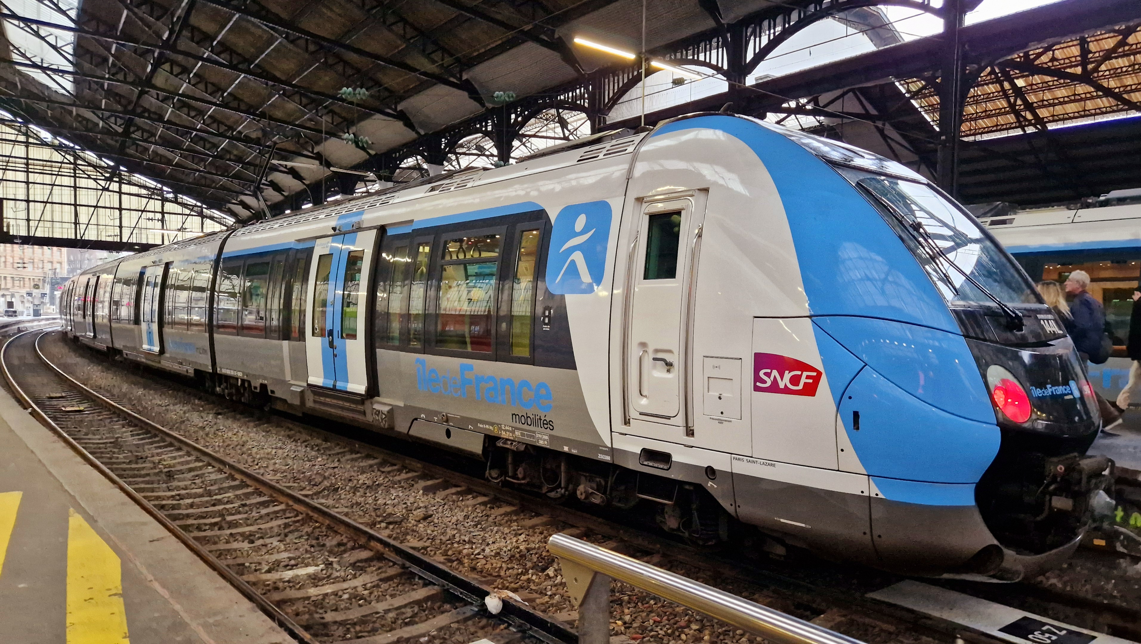 un treno regionale ile de france mobilites fermo al binario della gare saint-lazare, con la livrea bianca e azzurra e un passeggero che sale a bordo