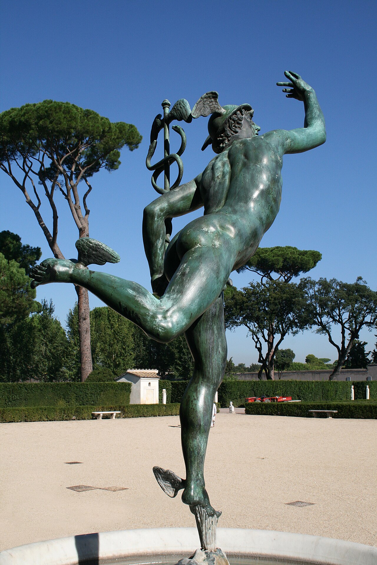 the bronze copy of giambologna s mercury on the fountain in front of the loggia, balanced on one foot with the leg raised behind and one arm up, with the pines of the garden in the background
